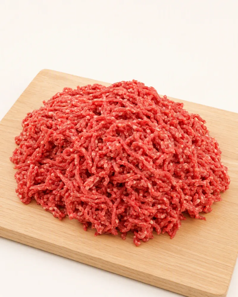 Porção de carne bovina moída crua, vermelha com pontos de gordura branca, sobre tábua de madeira clara